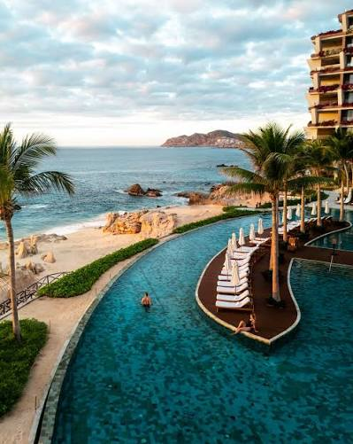 Curving beachfront resort pool with palm trees and ocean views