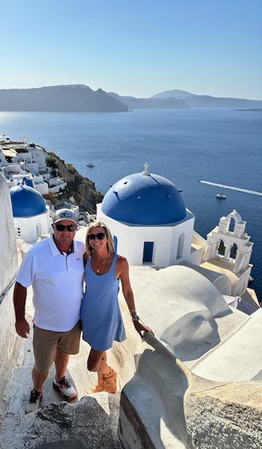 Nicole and her husband Jamie beside blue-domed buildings overlooking the sea in Greece