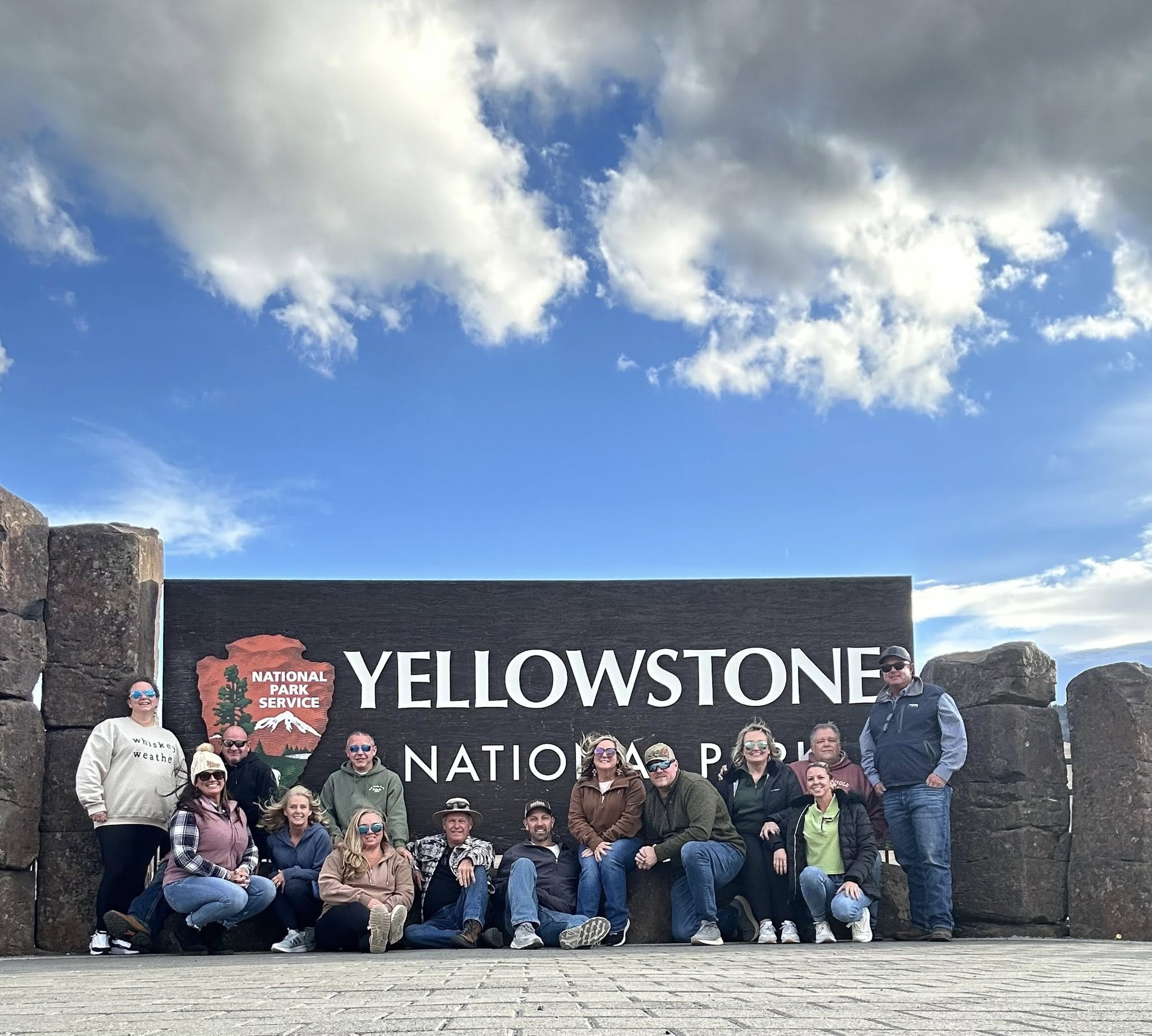 A group of travelers together at the Yellowstone National Park entrance sign